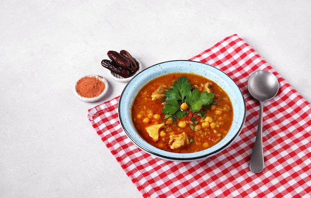 灰色のコンクリートのテーブルの上に青いボウルに入ったモロッコのハリラ スープと赤いナプキンのハリラはモロッコ料理
