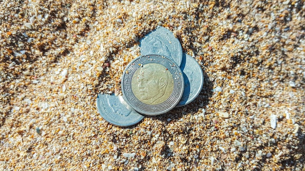 Марокканские деньги 5 дирхамов в песке Марокканские денежные монеты, частично зарытые в песок