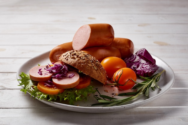 Mortadella with vegetables and herbs on a wooden plate on a wooden table.