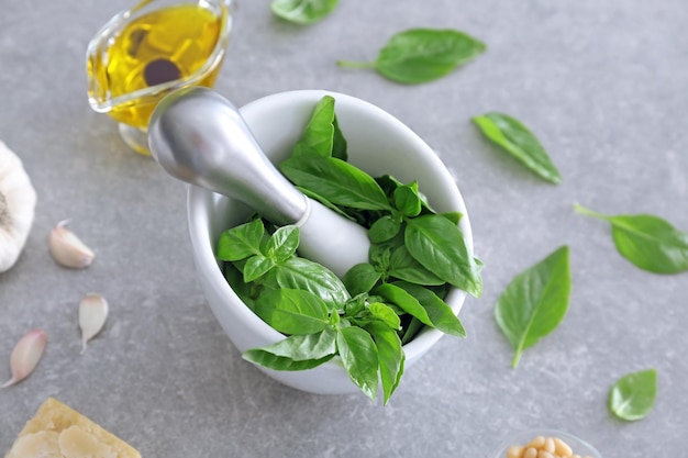 Mortar with pestle and basil leaves on table