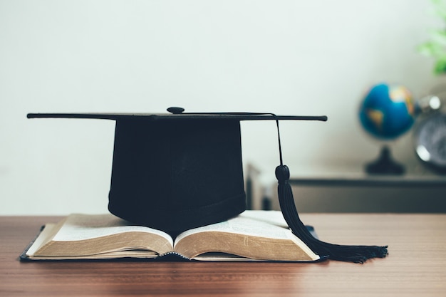 A mortarboard and graduation scroll on open books on the\
desk.education learning concept