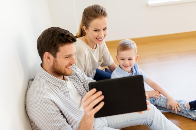 Photo mortgage, people, housing and real estate concept - happy family with tablet pc computer moving to new home