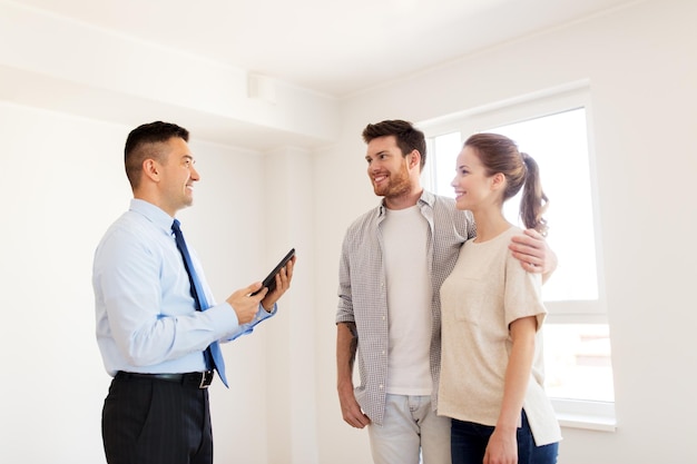 mortgage, people and real estate concept - happy couple and realtor with tablet pc computer at new home