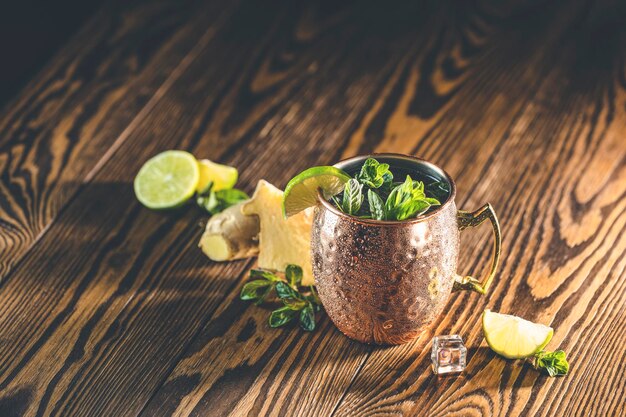 Photo moscow mule alcoholic cocktail in copper mug with crushed ice mint and lemon over minton dark wooden table with amazing backlight copy space