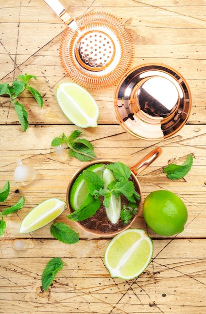Moscow mule alcoholic cocktail in copper mug with lime ginger beer vodka and mint Wooden bar counter bartender work tools top view