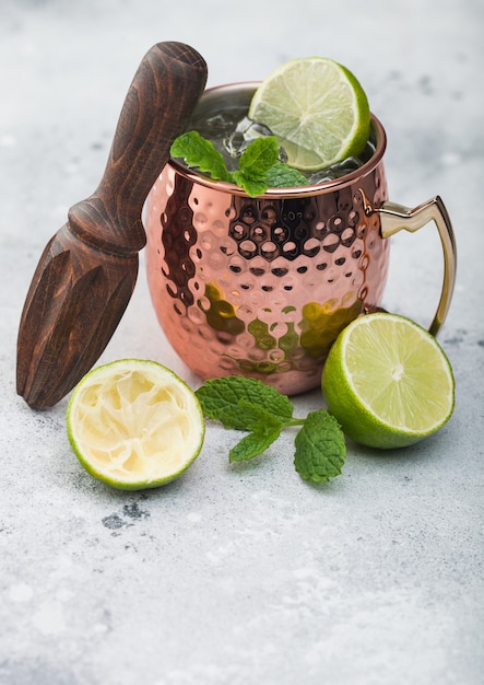 Moscow mule cocktail in a copper mug with lime and mint and wooden squeezer on light kitchen table background
