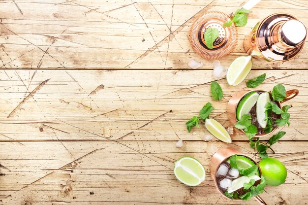 Moscow mule cocktails in copper mug with lime ice ginger beer vodka and mint Wooden background bar tools negative space topv view