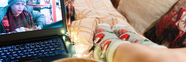 Moskou 11292021 film kijken quothome alonequot op een laptop thuis in knus bed met gloeiende lichtslinger 's nachts op kerst- of oudejaarsavond vrouwenbenen in wollen sokken en popcorn spandoek