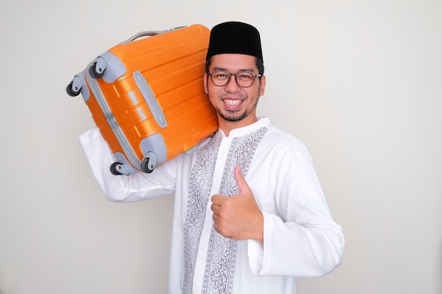 Moslem Asian man smiling at camera and give thumb up while bring a luggage