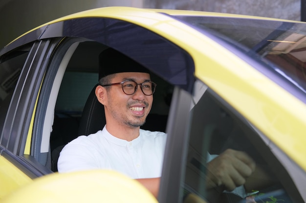 Мусульманский азиат счастливо улыбается за рулем своей машины