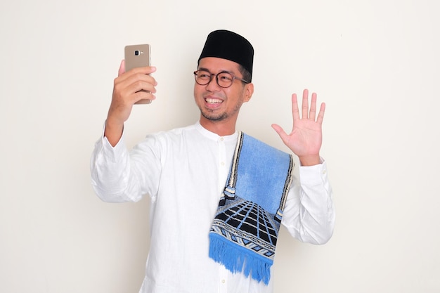 Photo moslem asian man smiling and waving hand during video call