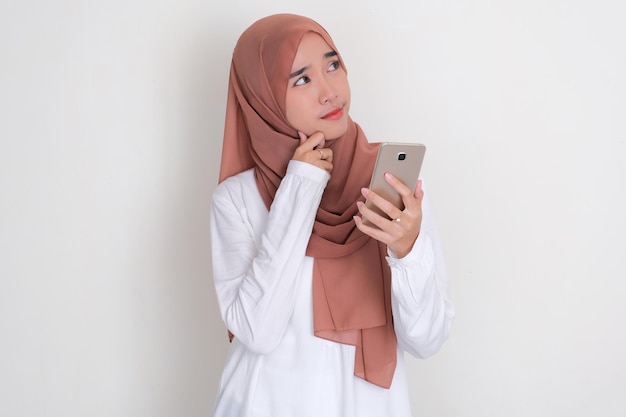 Moslem Asian woman thinking something while holding mobile phone