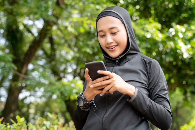 Moslim Aziatische vrouw die lacht tijdens het gebruik van haar smartphone tijdens het sporten buiten