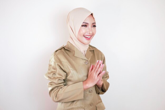 Moslim burgerarbeider draagt bruin uniform en hijab groet met een handgebaar en lacht naar de camera