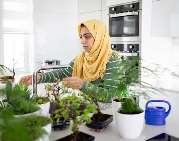 Moslim huisvrouw thuis planten in de keuken water geven