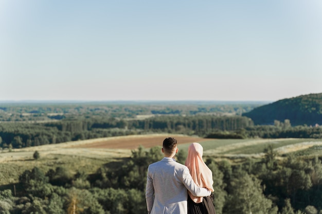 Moslim liefdesverhaal. Gemengd paar glimlacht en knuffels op de groene heuvels.