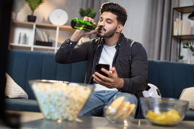 Moslim man met smartphone en bier voetbal kijken