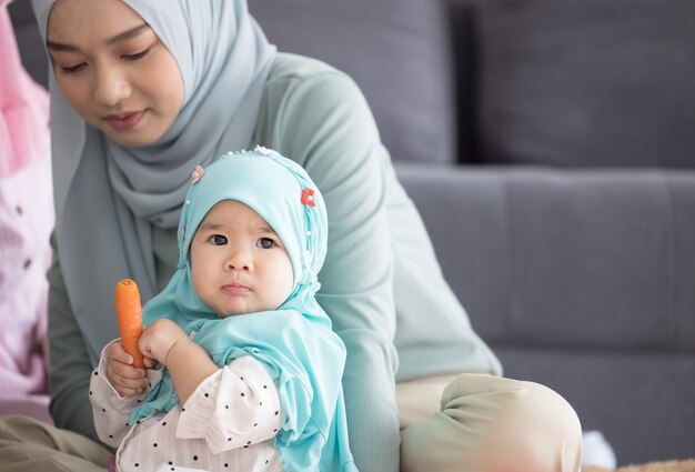 Moslim moeder in hijab is haar dochtertje in de woonkamer, liefdevolle relatie