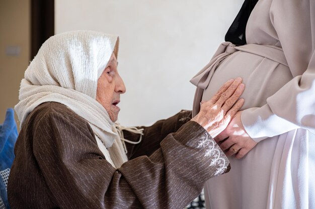 Moslim oude vrouw voelt zich opgewonden voor haar nieuwe kleinzoon raakt haar dochter buik om foetus bewegingen te voelen