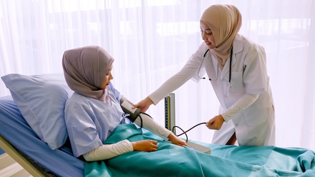 Moslim vrouwelijke arts die de bloeddruk van de patiënt controleert bij het ziekenhuisruimte.