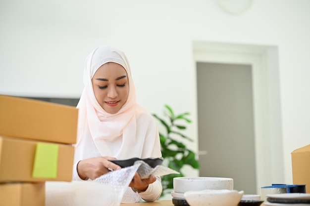 Moslim vrouwelijke online e-commerce ondernemer verpakt haar product in een kartonnen doos