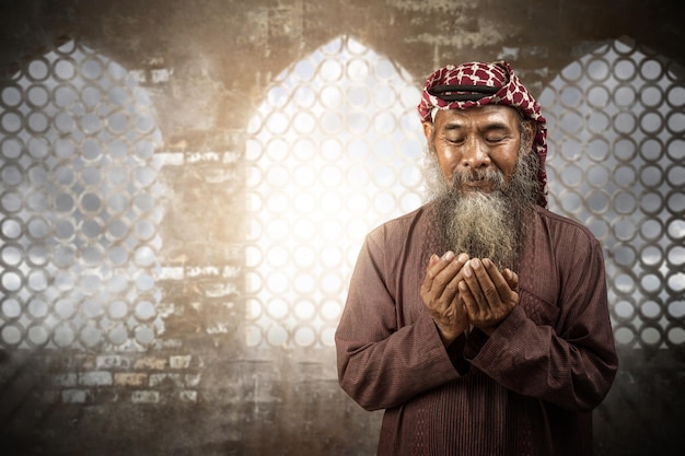 Moslimman met een baard die keffiyeh draagt met agal tijdens het bidden terwijl hij zijn handen opsteekt