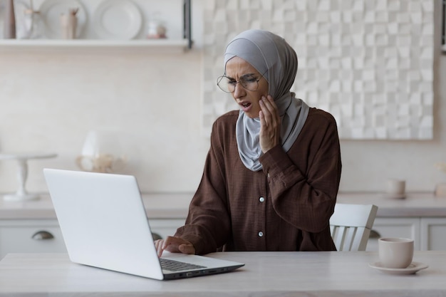 Moslimvrouw kiespijn thuis zakenvrouw in hijab die op afstand werkt vanuit huis zittend in de