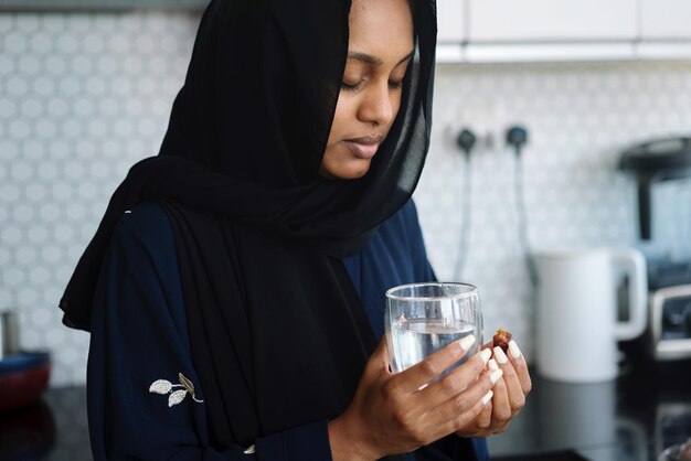 Moslimvrouw met abaya die tijdens de ramadan het vasten breekt, dadels eet en water drinkt