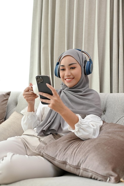 Moslimvrouw met hijab en koptelefoon die naar muziek luistert terwijl ze koffie drinkt