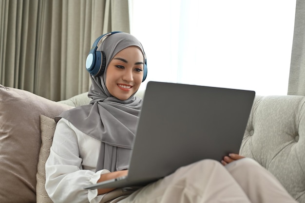 Moslimvrouw met hijab en koptelefoon kijken naar film op laptop