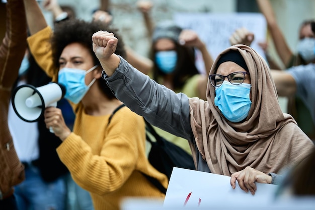 Moslimvrouw met opgeheven vuist die beschermend gezichtsmasker draagt terwijl ze deelneemt aan openbare demonstraties