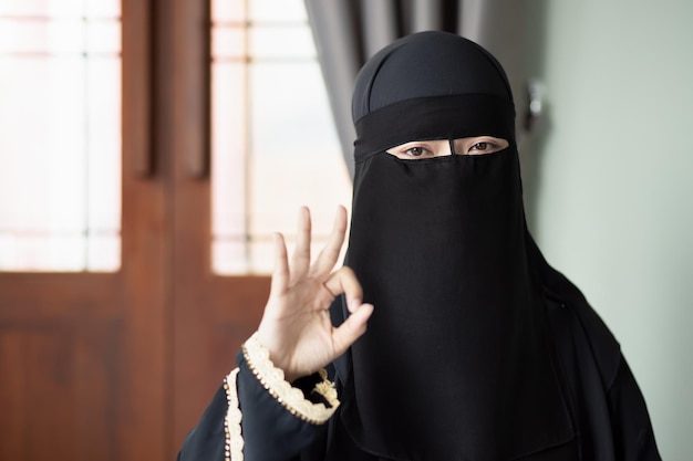 Moslimvrouw uit het Midden-Oosten met een gezichtsbedekkende sluier die wijst op goedkeuring ok handtekengebaar