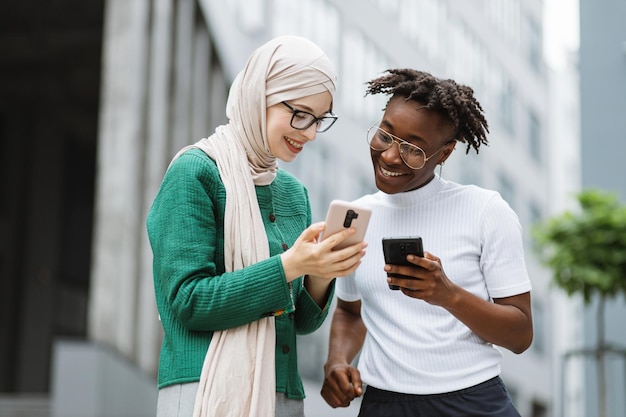 Moslimzakenvrouw in groen jasje die iets op smartphone laat zien aan haar vrouwelijke collega