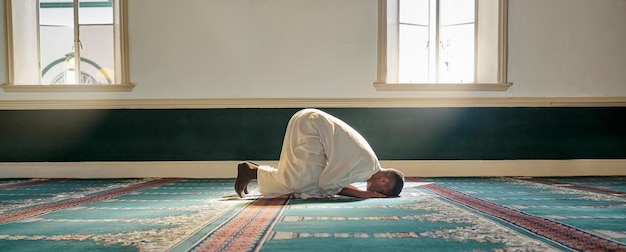 Mosque worship and muslim man in prayer on his knees for gratitude support or ramadan for spiritual wellness Religion tradition and islamic guy praying or reciting quran to allah at islam temple