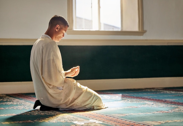 Photo mosque worship and muslim man in prayer on his knees for gratitude support or ramadan for spiritual wellness religion tradition and islamic guy praying or reciting quran to allah at islam temple