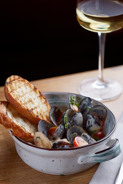 Mosselen met gegrild brood en glas witte wijn op houten tafel smakelijke zeevruchten concept met donkere achtergrond