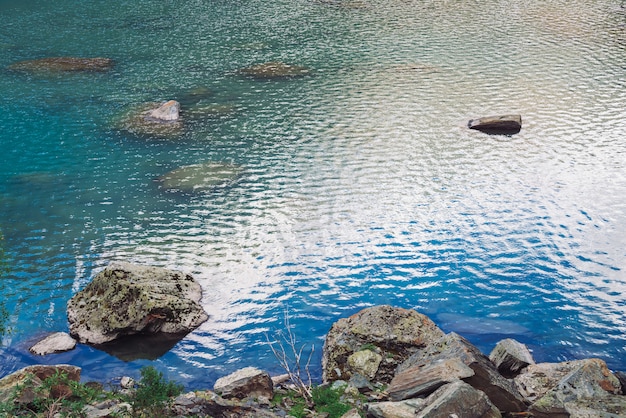 Pietre muschiose nel lago di montagna lucido. pulisca la superficie dell'acqua blu in altopiani nel giorno soleggiato con lo spazio della copia. lago roccioso roccioso con piante. luce del sole.