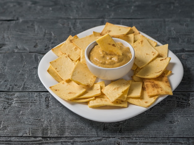 Mosterd met Mexicaanse tortillachips in een witte plaat op een houten tafel