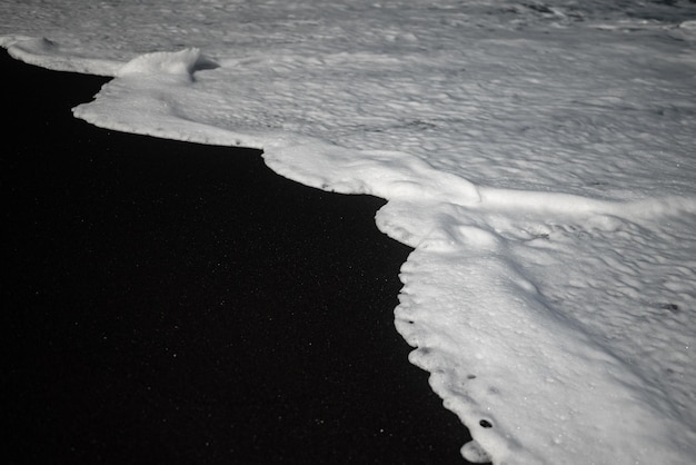 Mostly blurred black sand beach with white foam of sea waves White and black background with copy space Exotic black beach photo Dark volcanic sand and white ocean waves