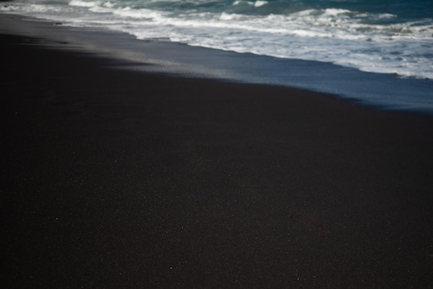 Mostly blurred black sand beach with white foam of sea waves White and black background with copy space Exotic black beach photo Dark volcanic sand and white ocean waves