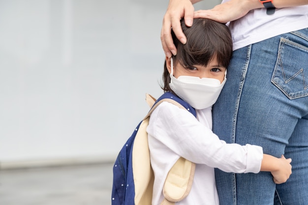 Mother accompanies the child to school. mom supports and motivates the student. the little girl wearing a face mask does not want to leave her mother. fears primary school.