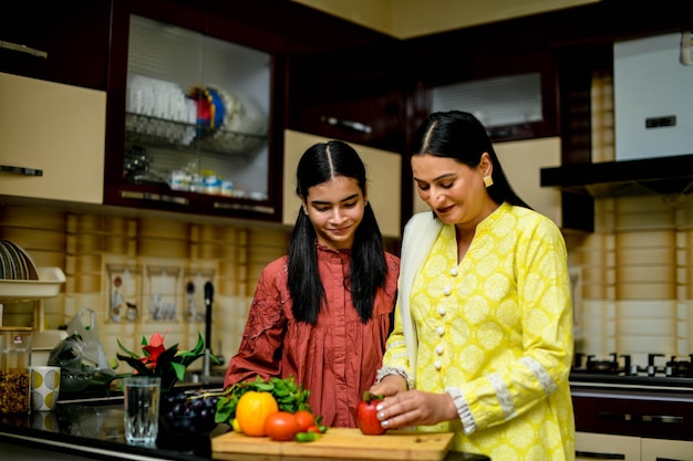 mother and adorable daughter cutting apple in kitchen indian pakistani model