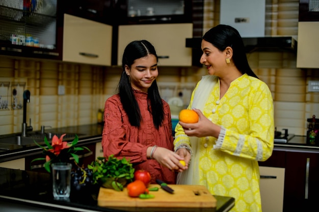 mother and adorable daughter holding fruits in kitchen indian pakistani model