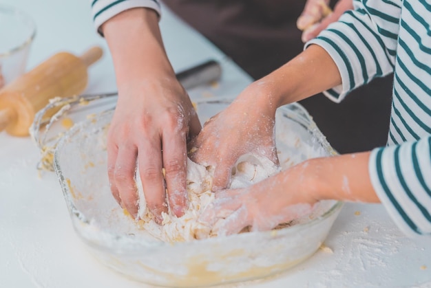 写真 母と子の手が一緒に働いて、家庭の台所でパン屋の料理とベーキングのために小麦粉と材料を混ぜ合わせます