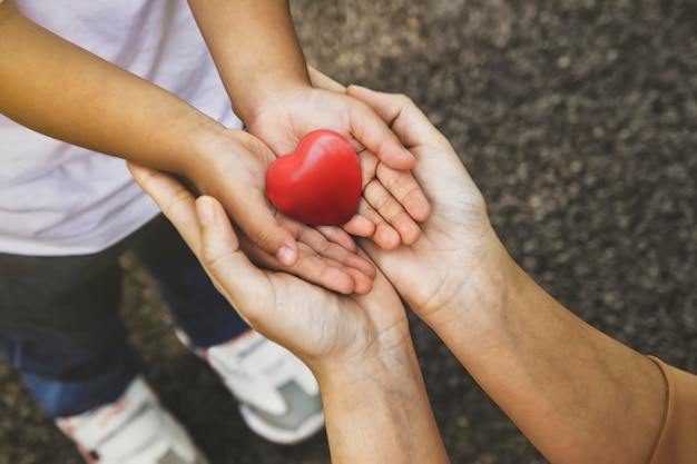 写真 母と子の手は、母性と純粋な愛を気遣う愛の赤いハートを保持します。