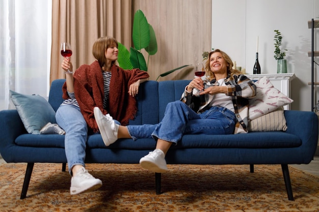 Фото Мать и дочь сплетничают, попивая вино, сидя на диване