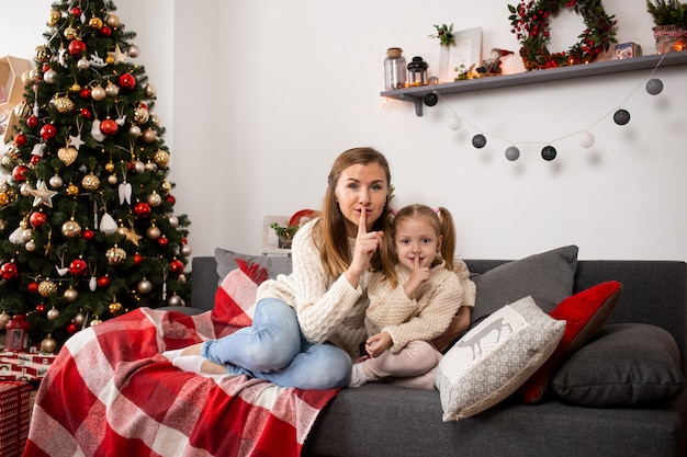 母と少女は自宅でクリスマスイブにクリスマスツリーの近くで遊んでリラックスします。