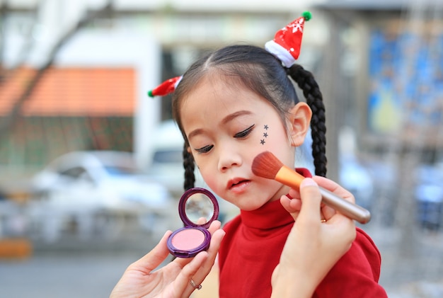 Mother applying makeup on her daughter face.