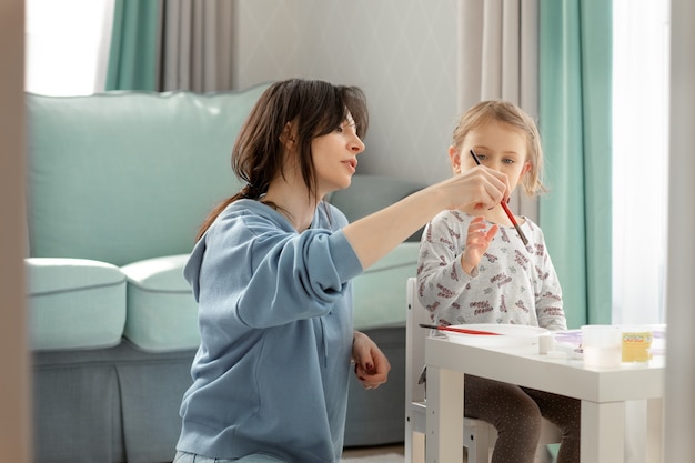 Mother or an art teacher is teaching the child to drawing and holding the brush correctly