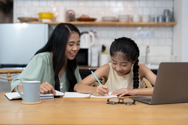 Mother and asian kid little girl learning on laptop computer making homework studying knowledge with online education elearning system children video conference with teacher tutor at home